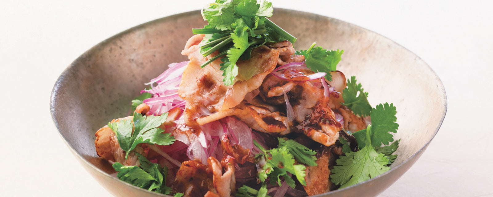 A bowl of Thai-inspired spicy dashi pork salad with red onions and fresh cilantro.