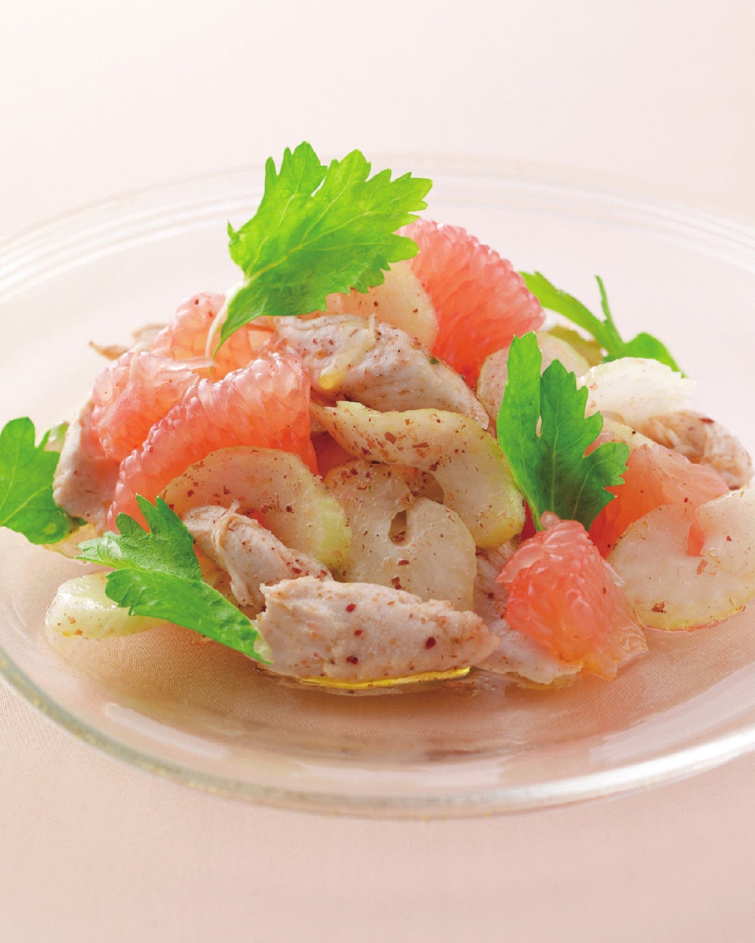 A bowl of grapefruit salad with chicken slices and fresh herbs.
