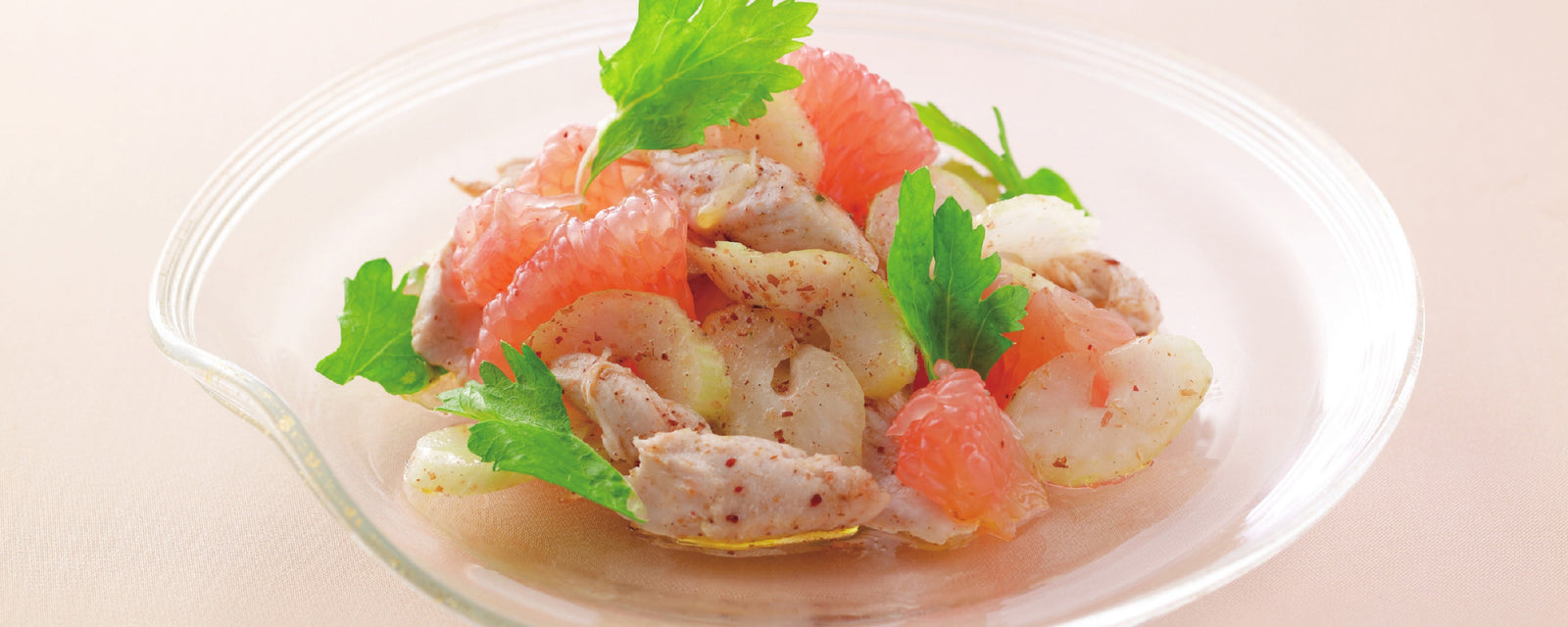 A bowl of grapefruit salad with chicken slices and fresh herbs.