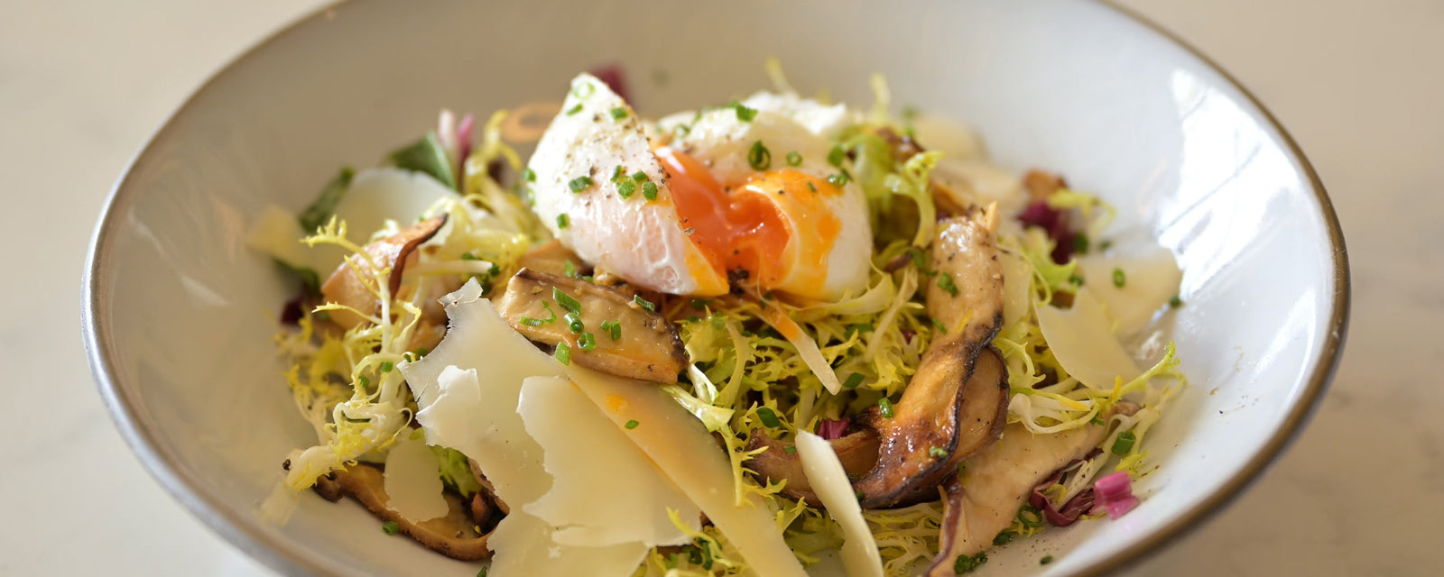 A bowl of mixed mushroom salad topped with a soft-poached egg and shaved cheese.