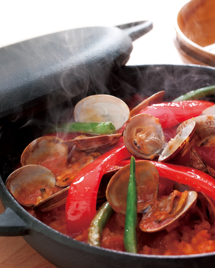 A skillet of seafood paella with clams, red peppers, and green beans.