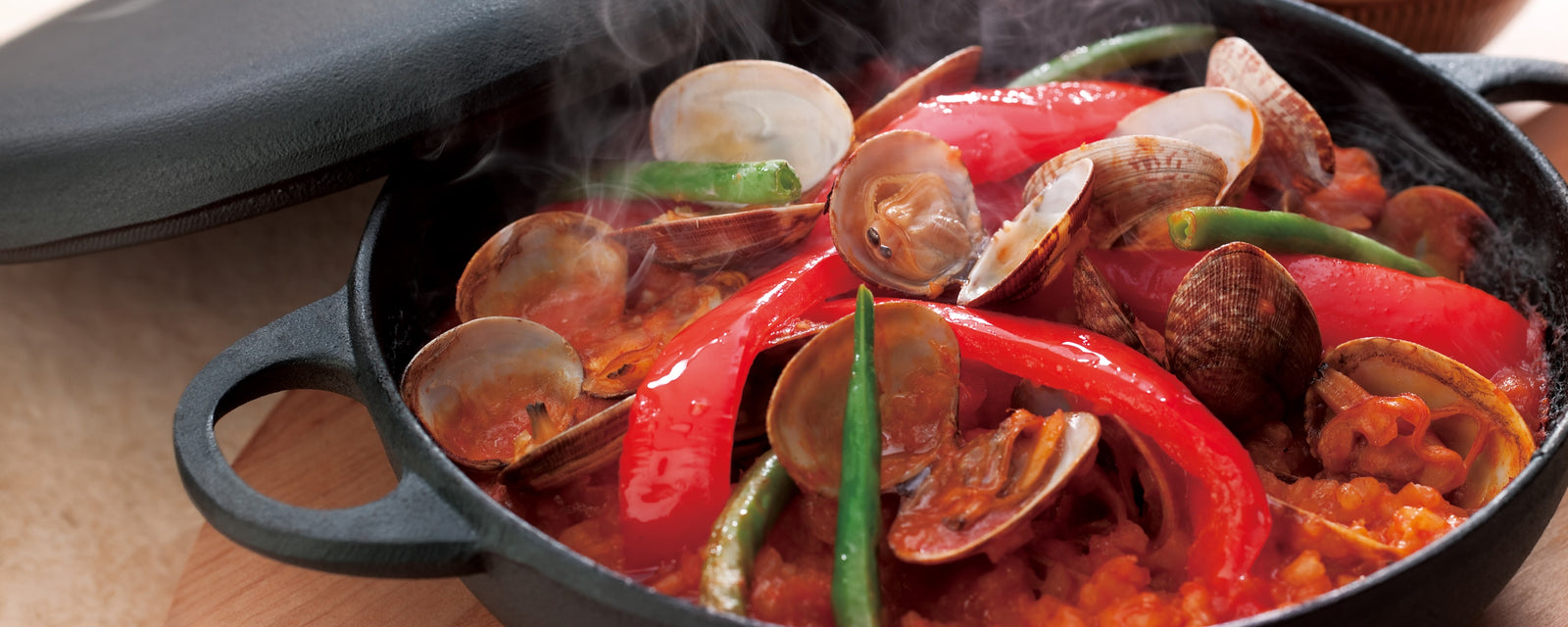 A skillet of seafood paella with clams, red peppers, and green beans.