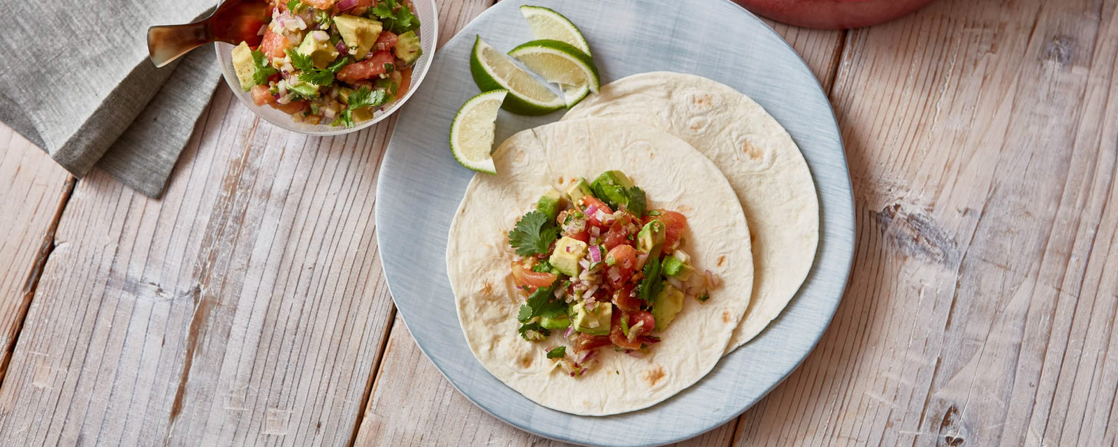 Tortillas topped with fresh salsa, avocado, and cilantro, served with lime wedges