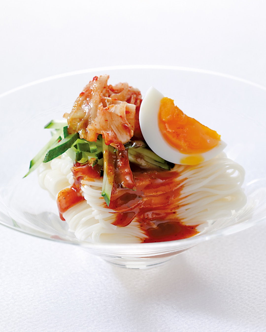 A bowl of bibim somen noodles topped with kimchi, cucumber, and a soft-boiled egg.