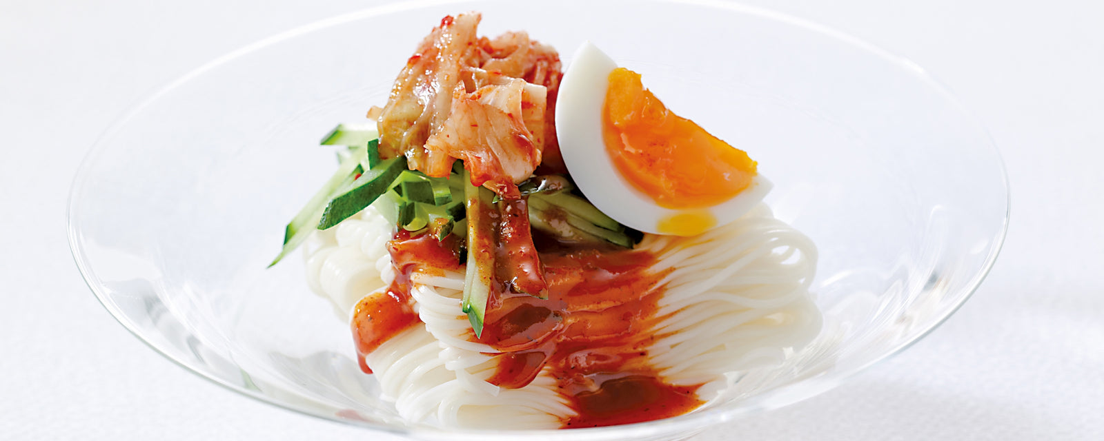 A bowl of bibim somen noodles topped with kimchi, cucumber, and a soft-boiled egg.