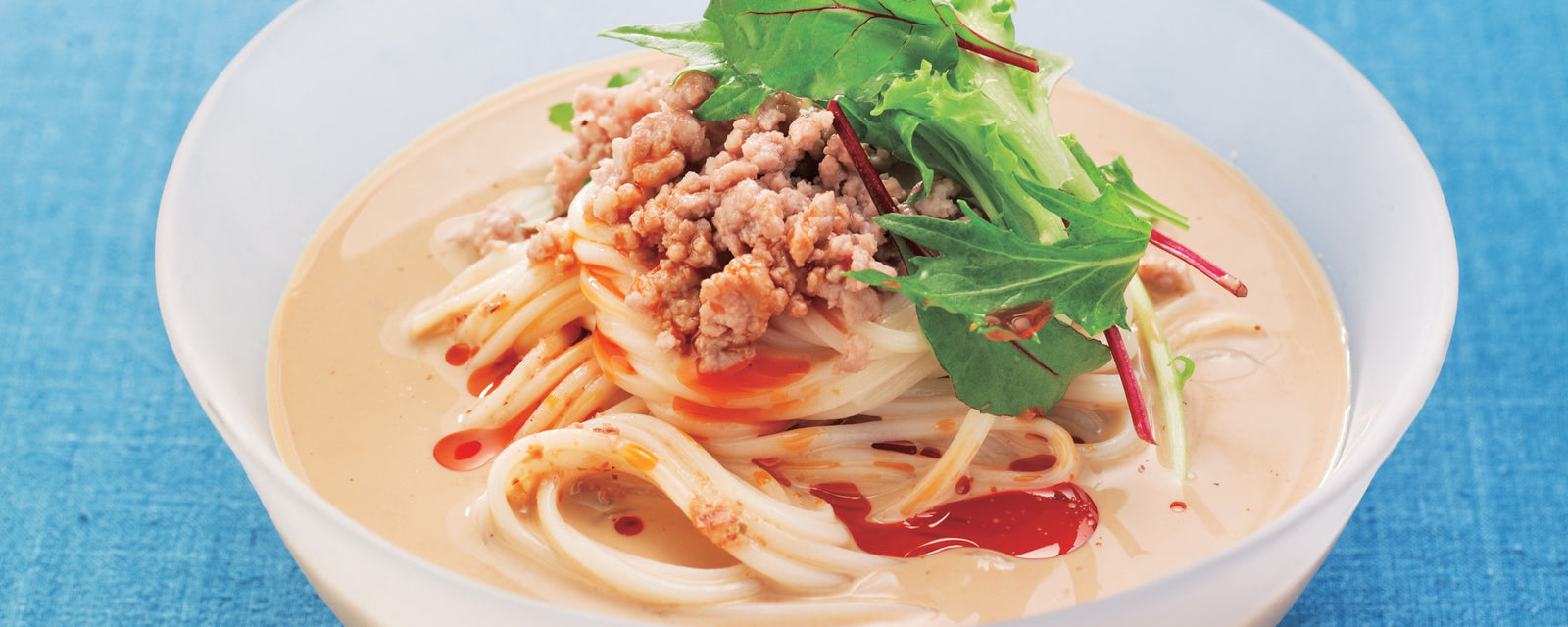A bowl of soy milk dandan noodles topped with minced meat and leafy greens.
