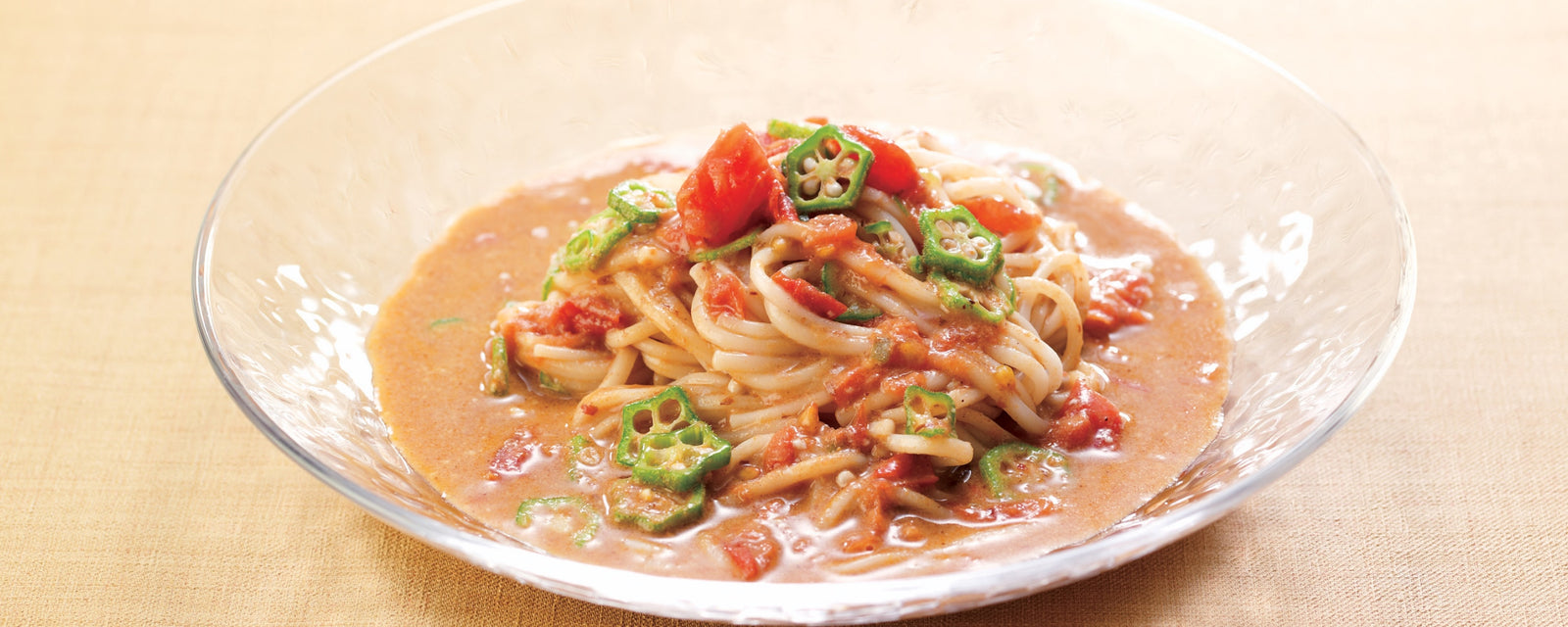 A bowl of coconut curry noodles topped with tomatoes and sliced okra.