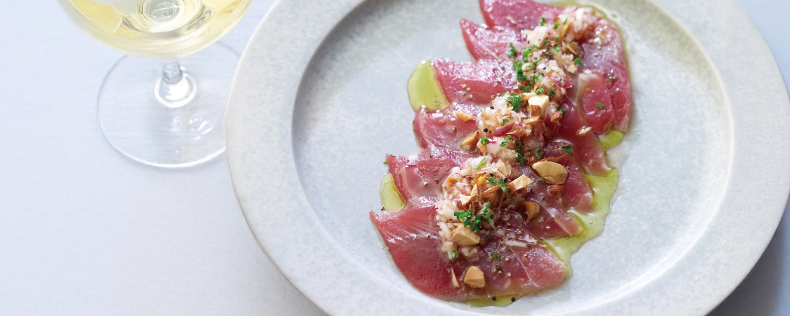 A plate of tuna carpaccio topped with chopped nuts, herbs, and olive oil.