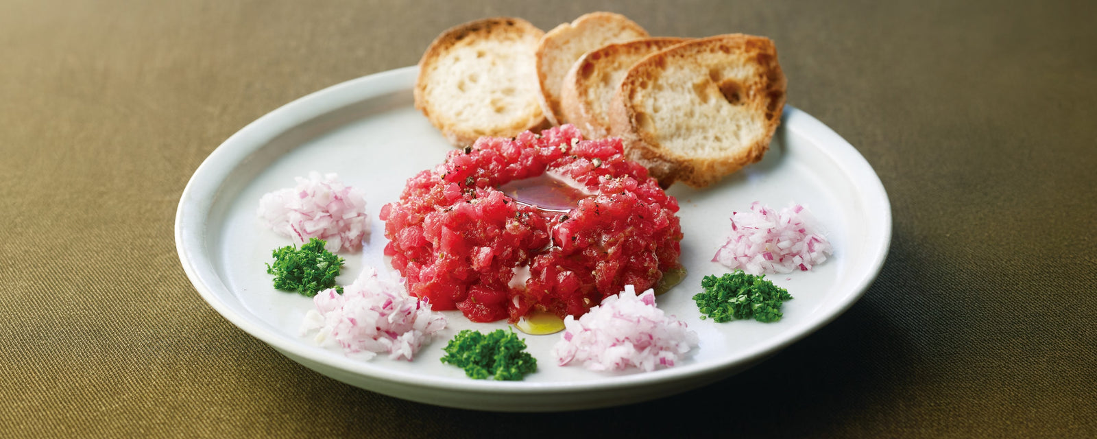 A plate of tuna tartare served with toasted bread slices and chopped herbs.