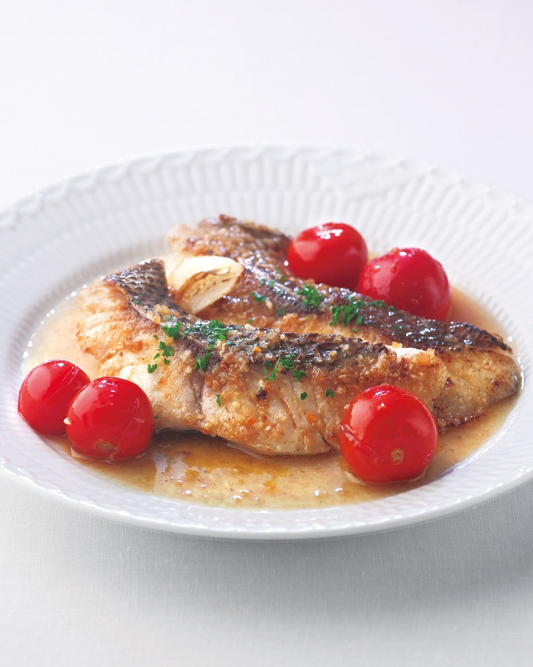 A plate of acqua pazza with white fish simmered in a light broth with cherry tomatoes.