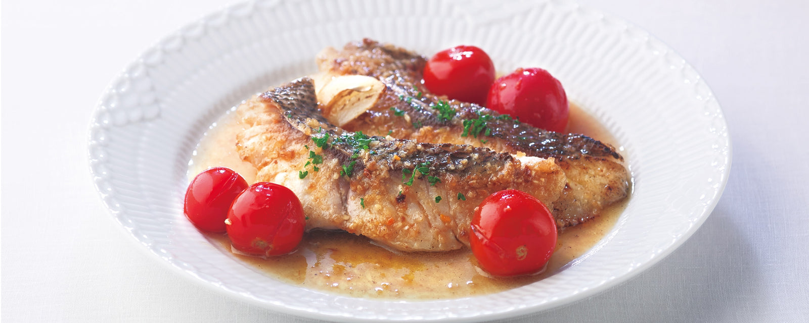A plate of acqua pazza with white fish simmered in a light broth with cherry tomatoes.