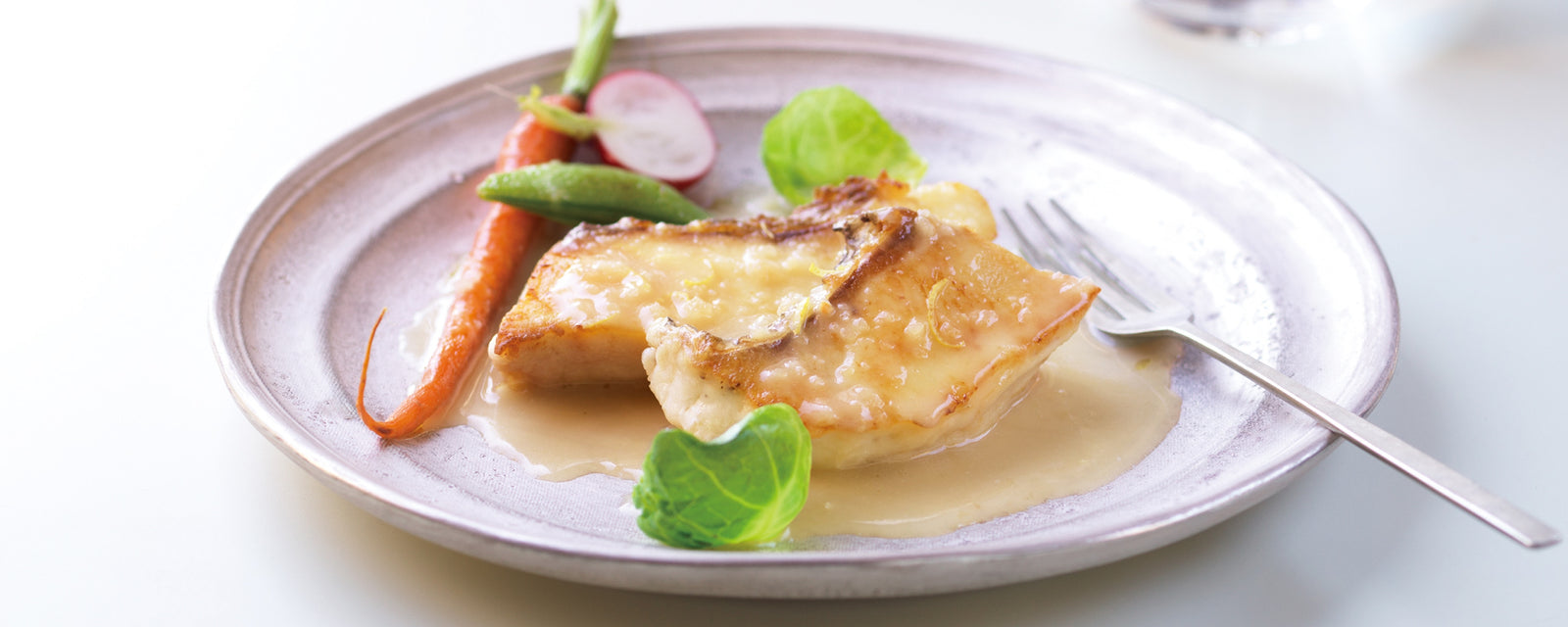 A plate of white fish topped with lemon butter sauce, served with fresh vegetables.