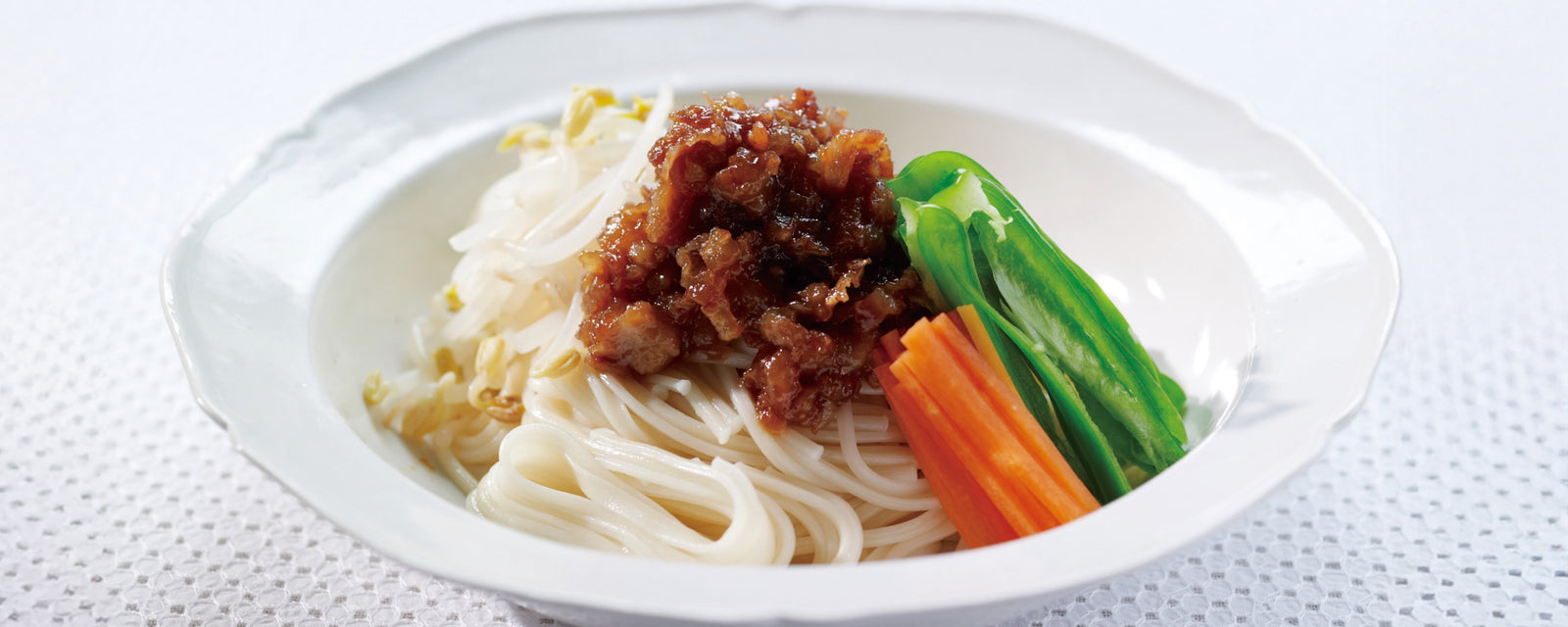 A bowl of zhajiang-style udon noodles topped with minced meat and vegetables.