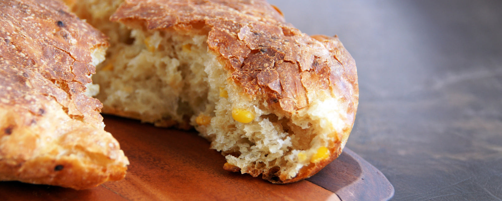A close-up of a sliced homemade bread roll with corn kernels inside.