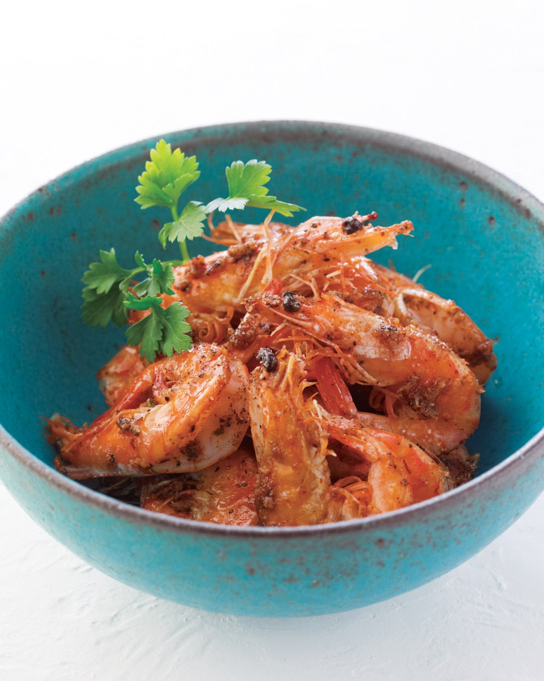 A bowl of black pepper shrimp garnished with fresh herbs.