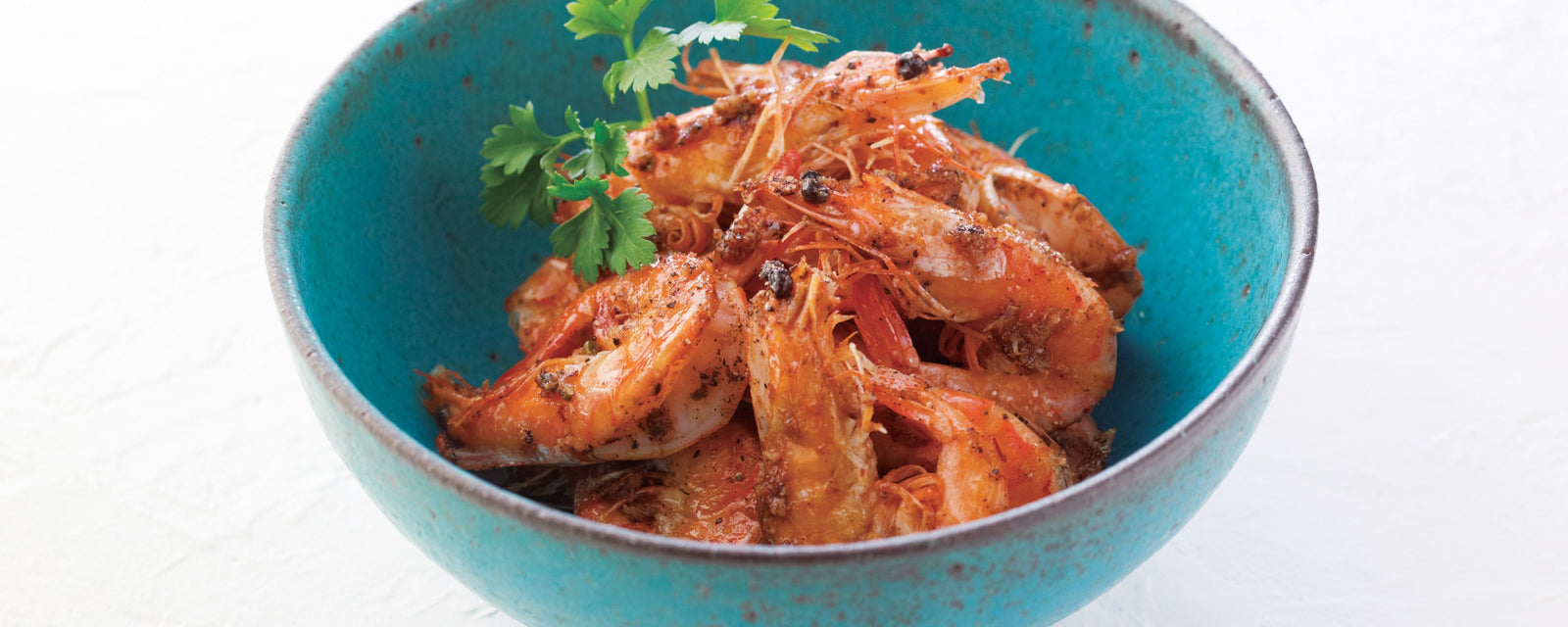 A bowl of black pepper shrimp garnished with fresh herbs.