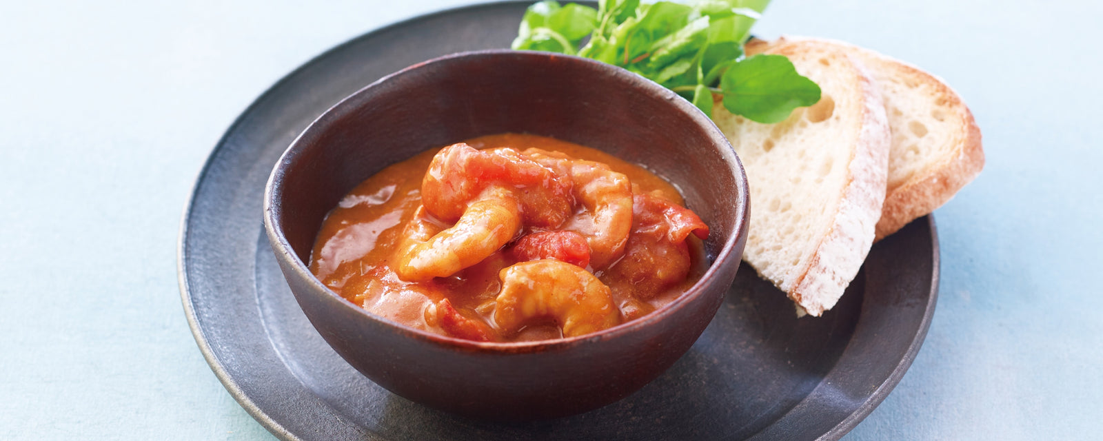 A bowl of shrimp in tomato sauce served with sliced bread on the side.