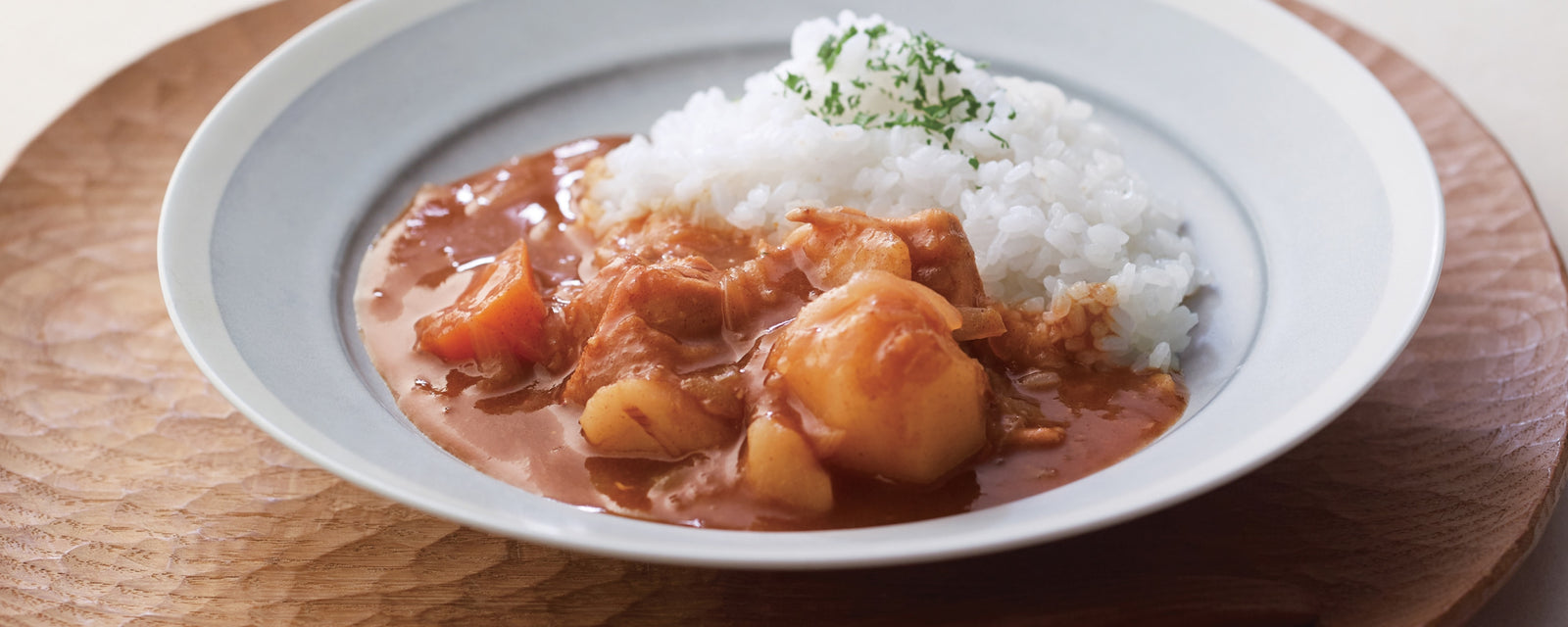 A plate of Japanese curry with chicken and potatoes served alongside steamed rice.