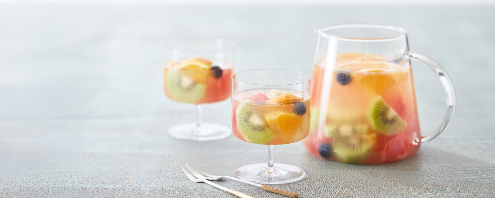 Fruit-infused drink with kiwi, citrus, and berries served in glasses and a pitcher