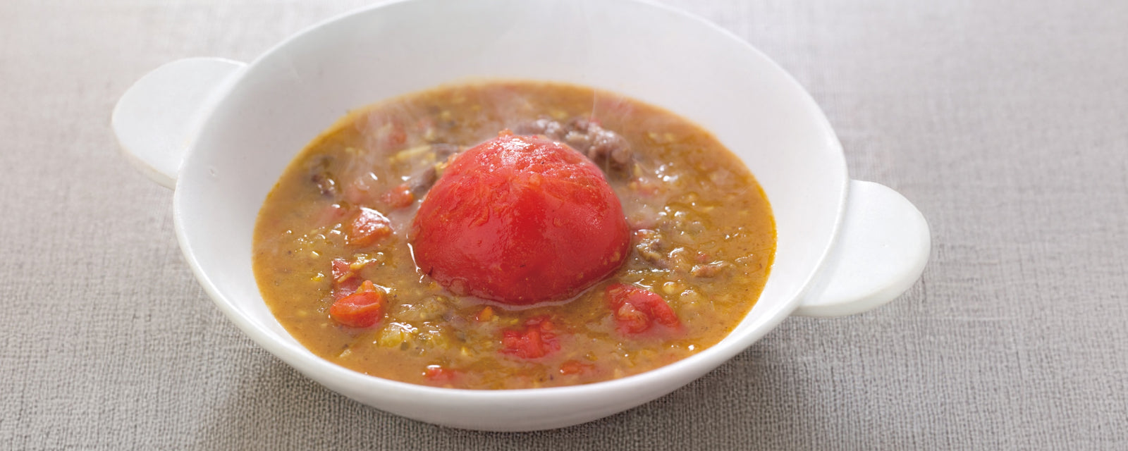 A bowl of hot tomato curry served with a whole peeled tomato on top.