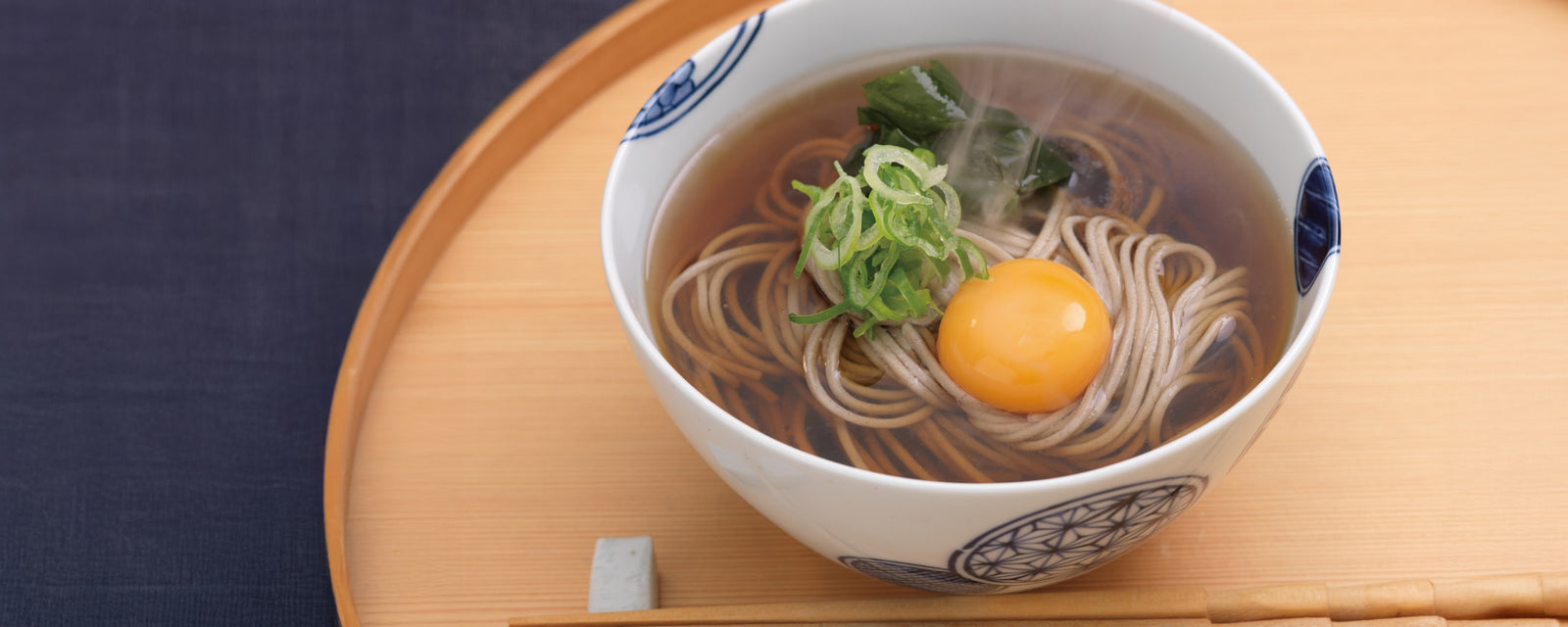 A bowl of hot Japanese soba noodles in broth topped with a raw egg yolk and green onions.