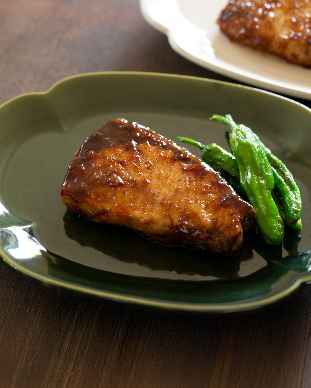 A grilled fish fillet glazed with teriyaki sauce, served with green peppers on a plate.