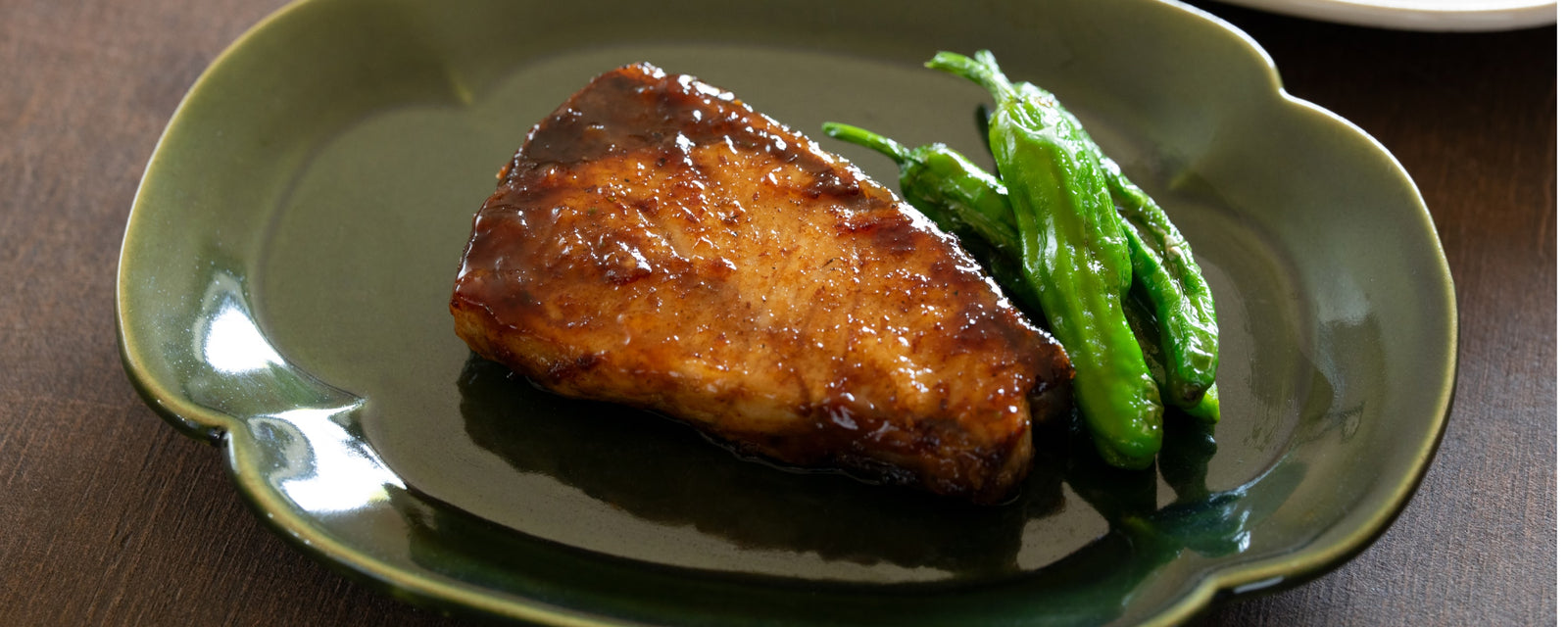 A grilled fish fillet glazed with teriyaki sauce, served with green peppers on a plate.