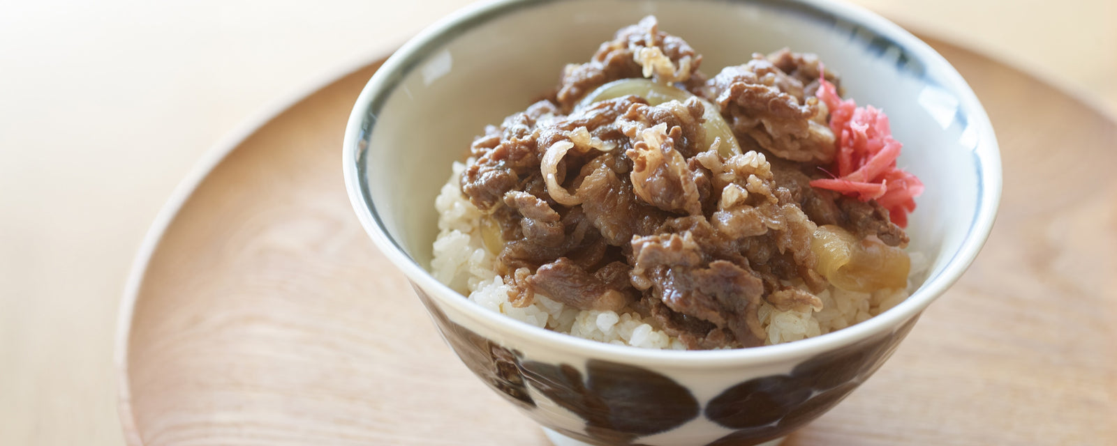 A bowl of Japanese beef gyudon served over steamed rice with pickled ginger.