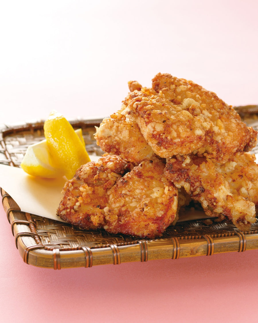 Crispy fried chicken pieces served on a bamboo tray with lemon wedges.