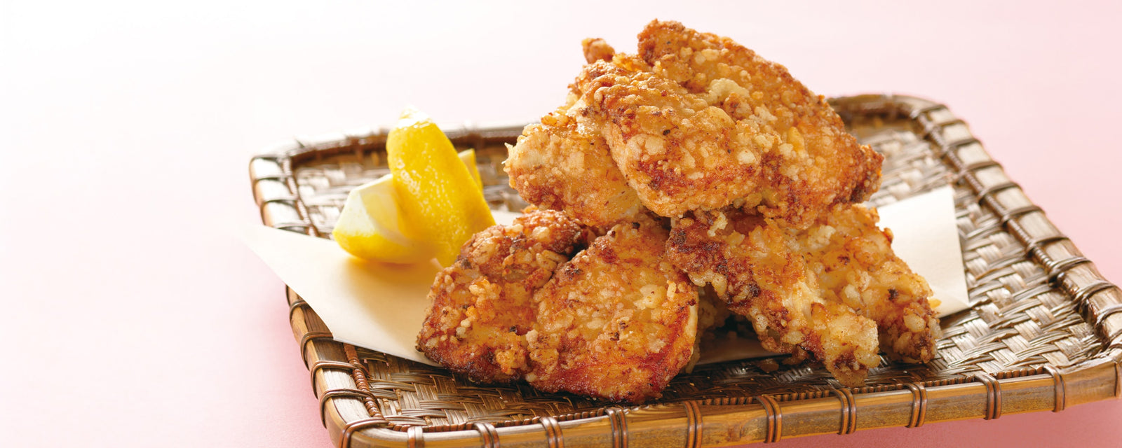 Crispy fried chicken pieces served on a bamboo tray with lemon wedges.