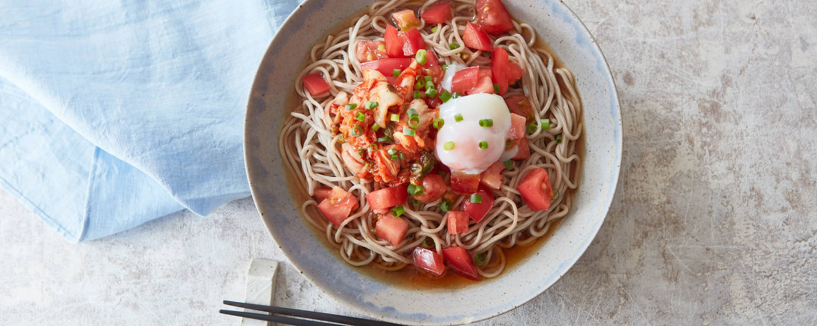 Cold soba noodles topped with kimchi, diced tomatoes, and a soft-poached egg