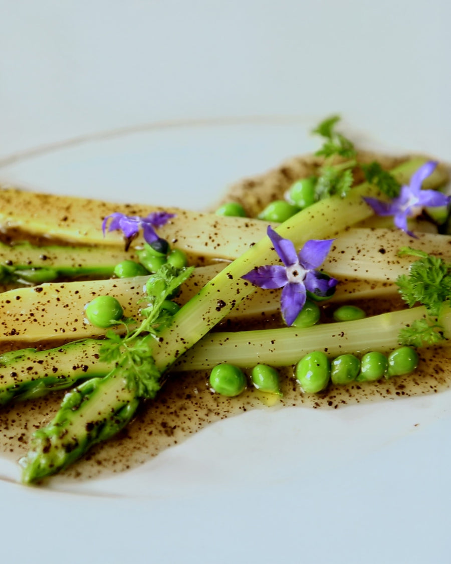 Asparagus with green peas and truffle oil, garnished with herbs and edible flowers.