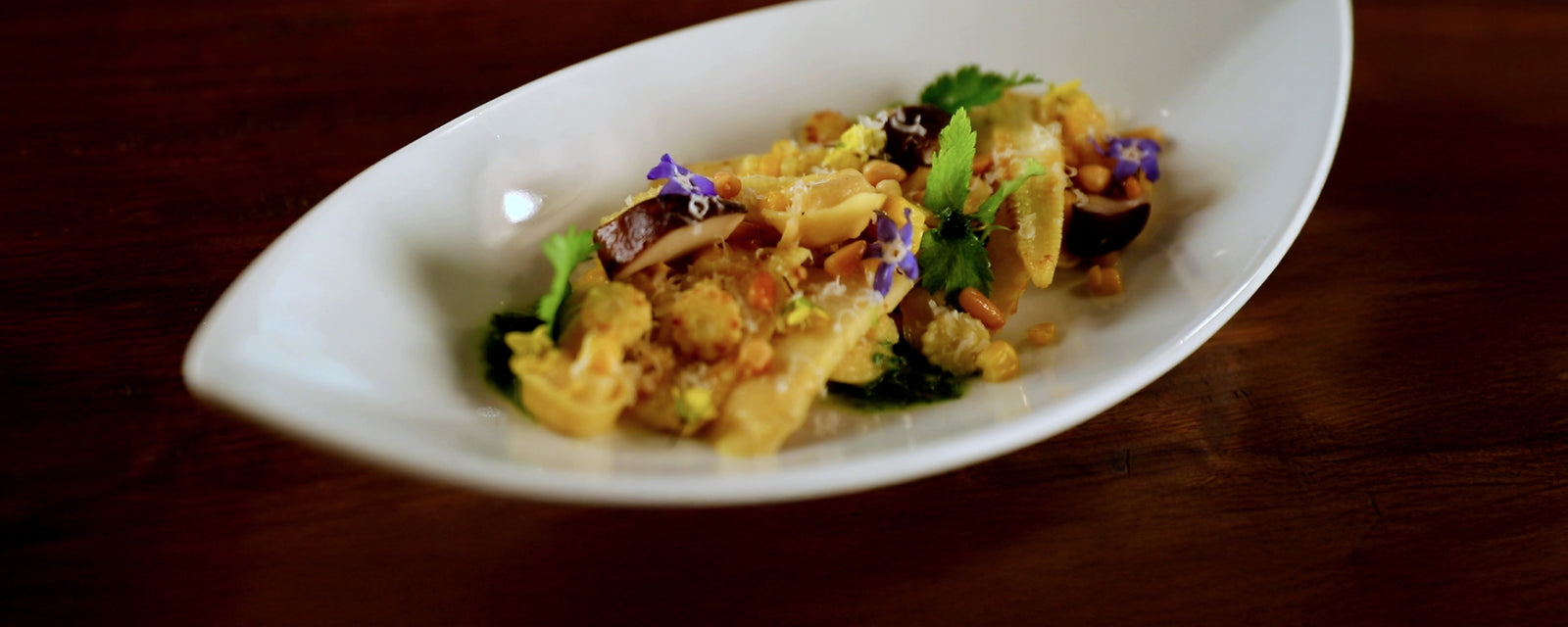 Tortellini with corn and bamboo shoots served with herbs on a white plate.
