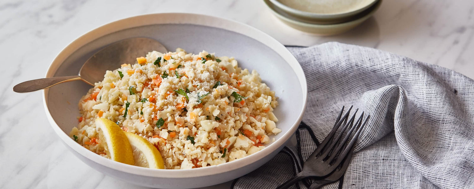 Cauliflower rice with diced vegetables, herbs, and lemon wedges on a plate