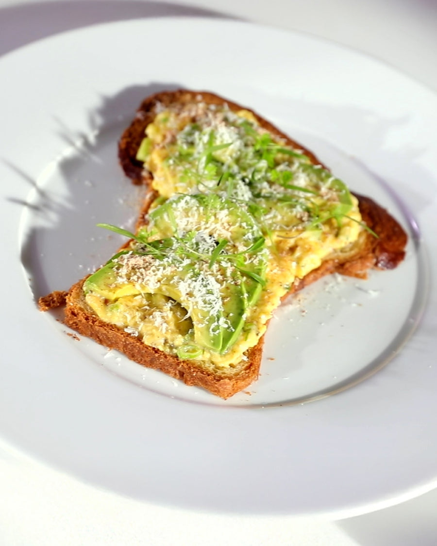Scrambled eggs and avocado served on toasted brioche, finished with grated cheese and herbs.