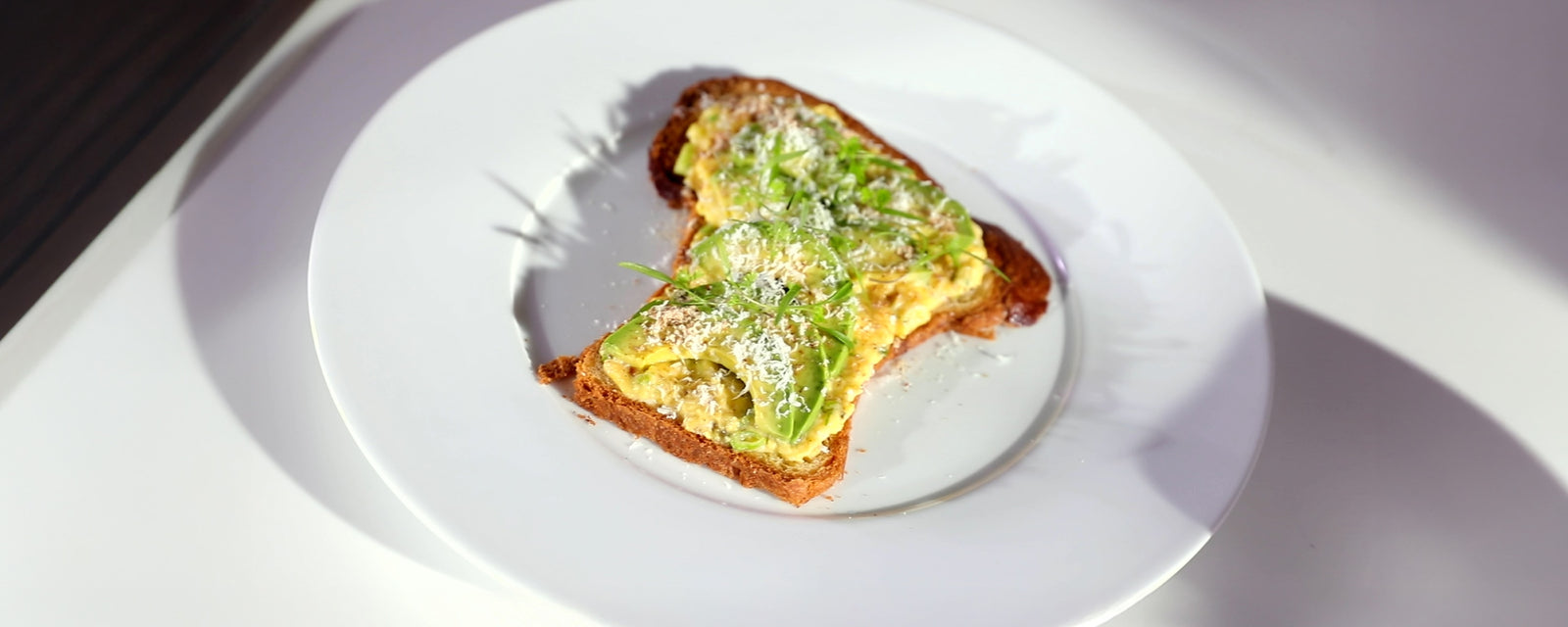 Scrambled eggs and avocado served on toasted brioche, finished with grated cheese and herbs.