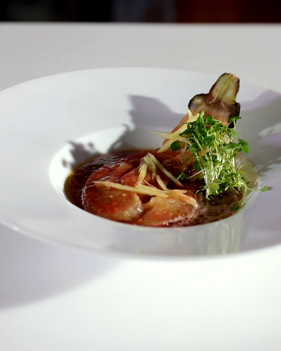 Fire-roasted eggplant served with a savory sauce and fresh greens in a shallow bowl.