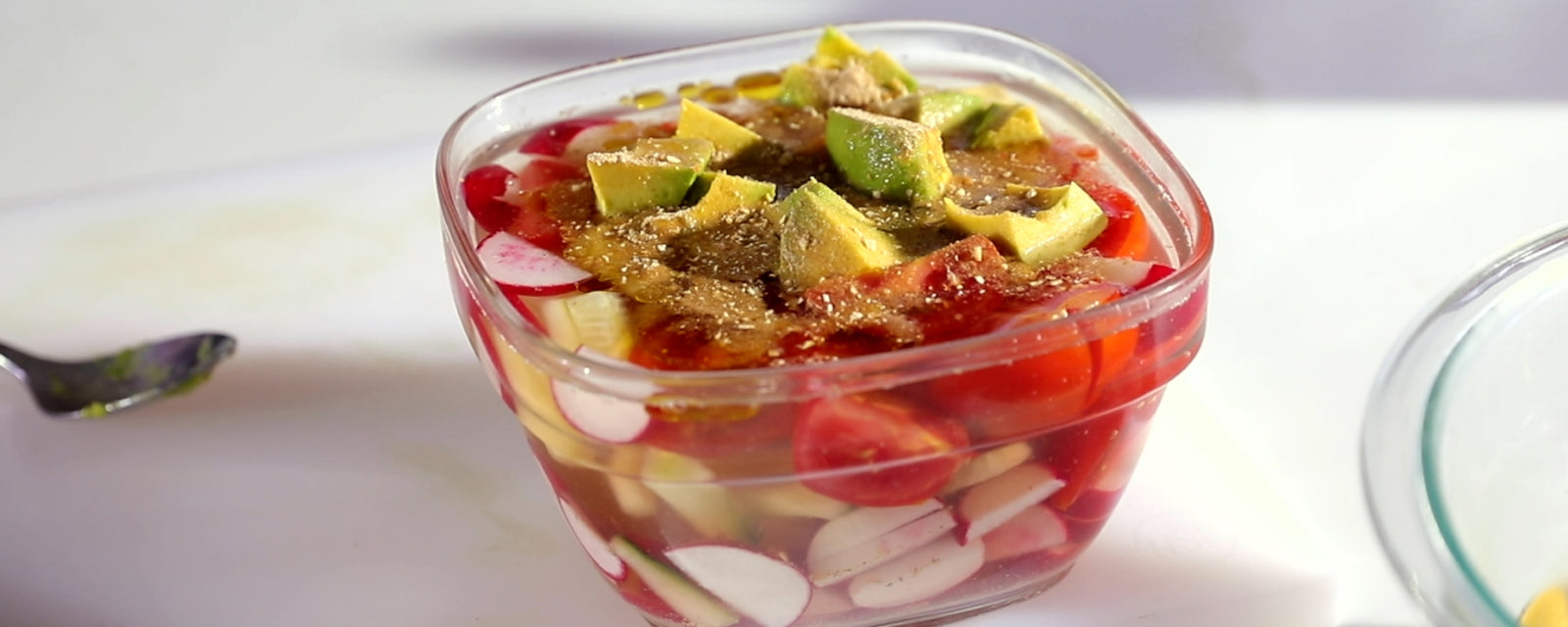 Chilled cucumber and red radish cold soup salad topped with avocado in a glass bowl.