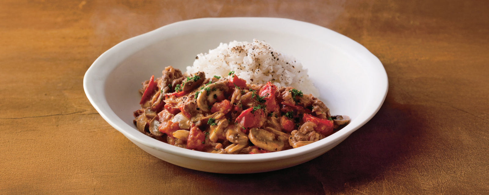 Beef stroganoff with mushrooms and tomatoes served alongside steamed white rice.