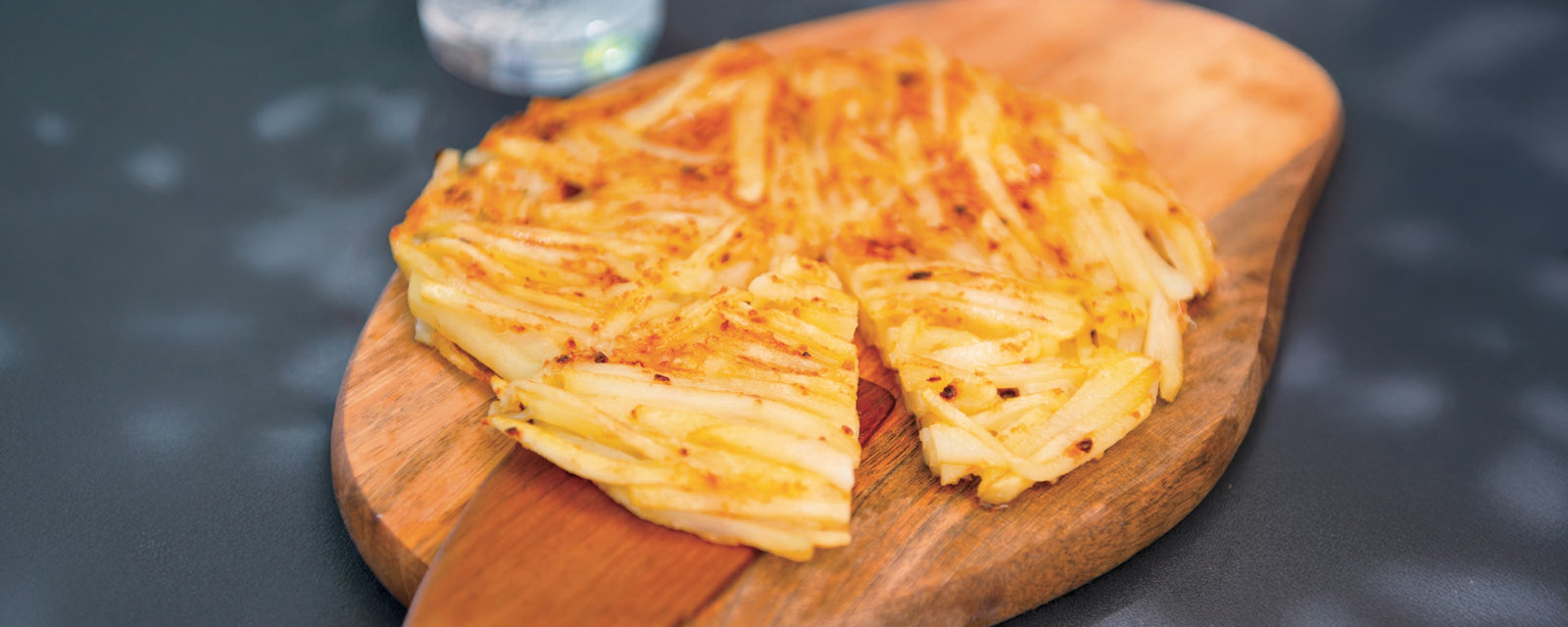 Crispy potato galette sliced on a wooden board, showing thin layers of potatoes.