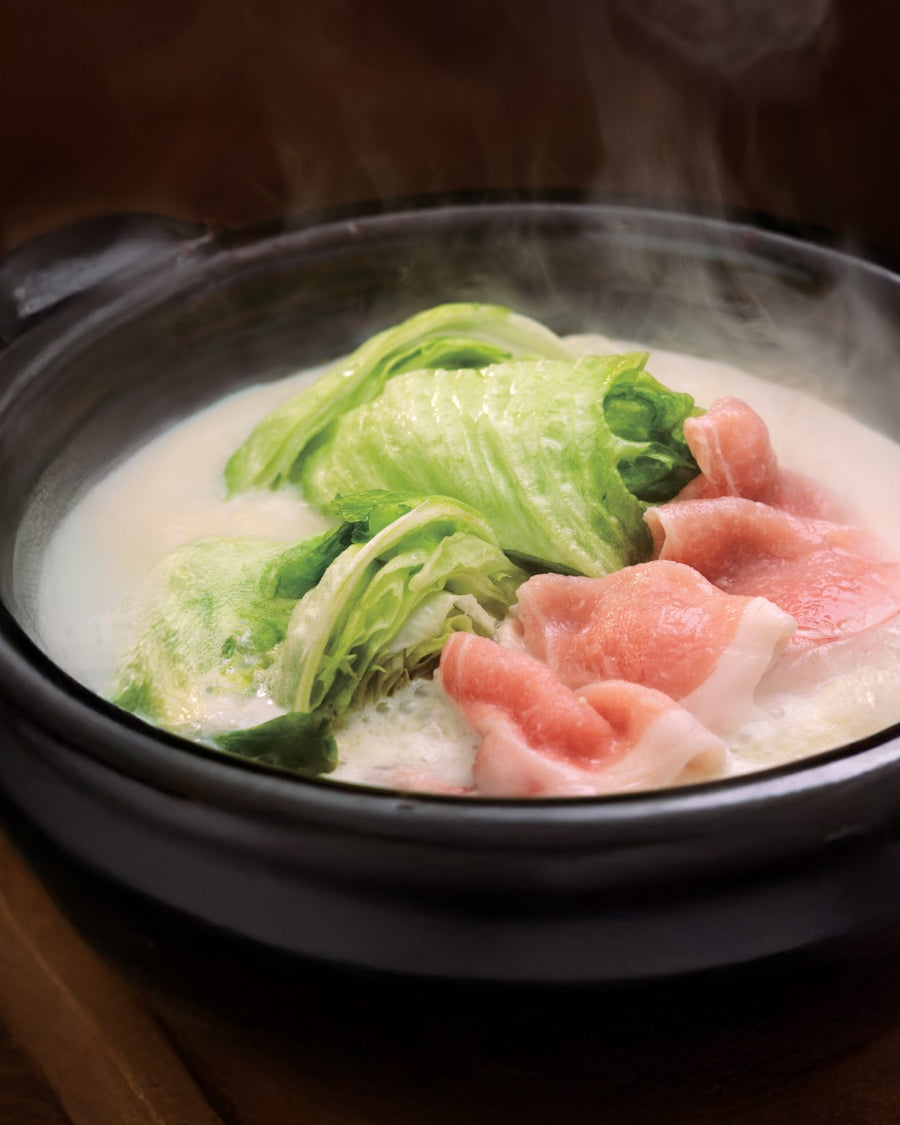 Soy milk hot pot with lettuce and thinly sliced pork simmering in a creamy broth.