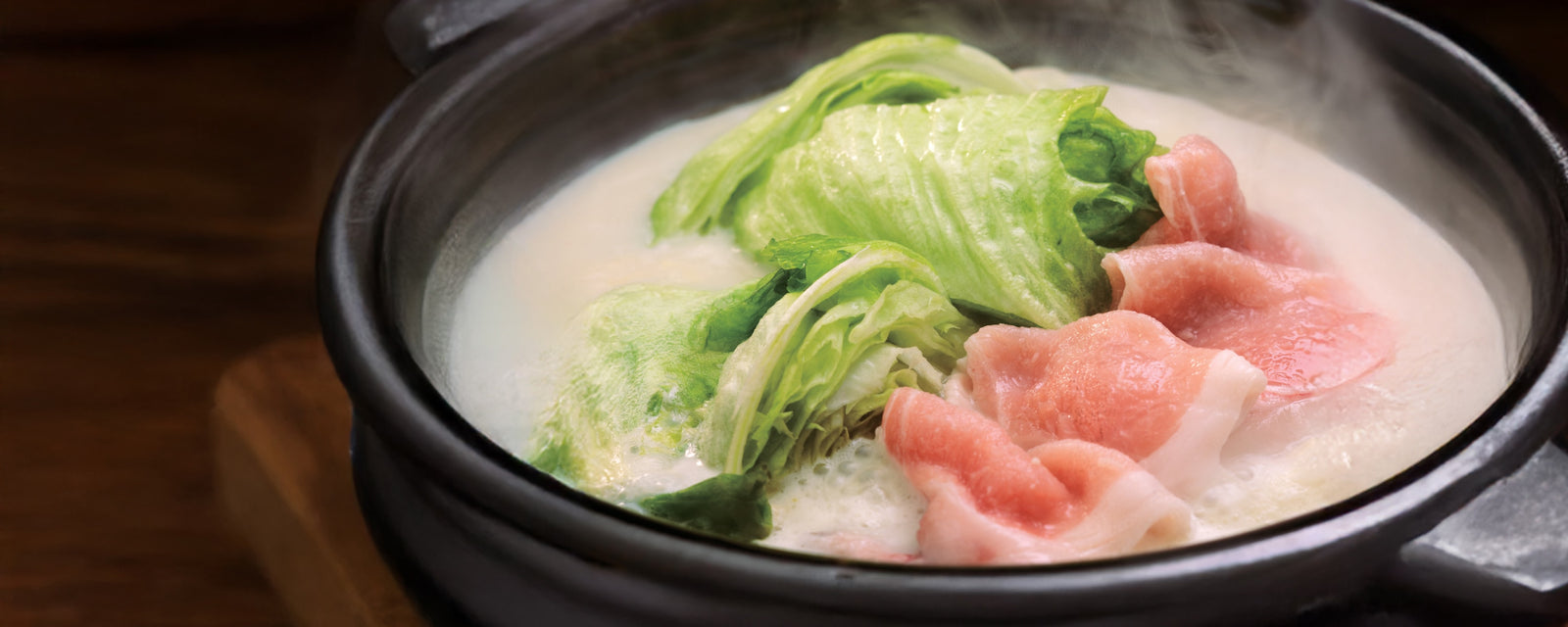 Soy milk hot pot with lettuce and thinly sliced pork simmering in a creamy broth.