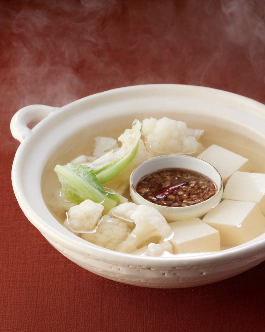 Steaming cauliflower yudofu with tofu cubes, served with celery sauce in a ceramic pot.
