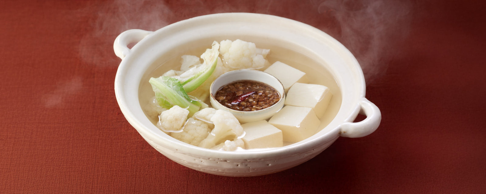 Steaming cauliflower yudofu with tofu cubes, served with celery sauce in a ceramic pot.