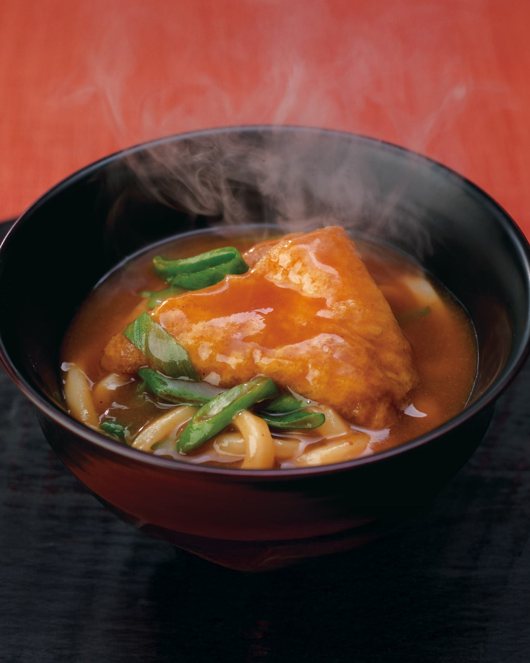 Steaming curry udon noodles topped with fried tofu and green onions in a bowl.