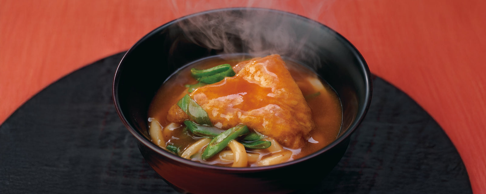 Steaming curry udon noodles topped with fried tofu and green onions in a bowl.