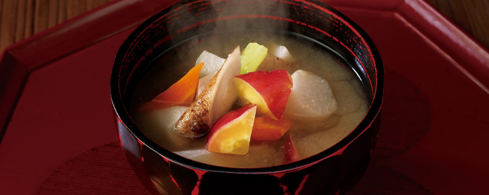 Steaming miso soup with assorted root vegetables served in a lacquer bowl.