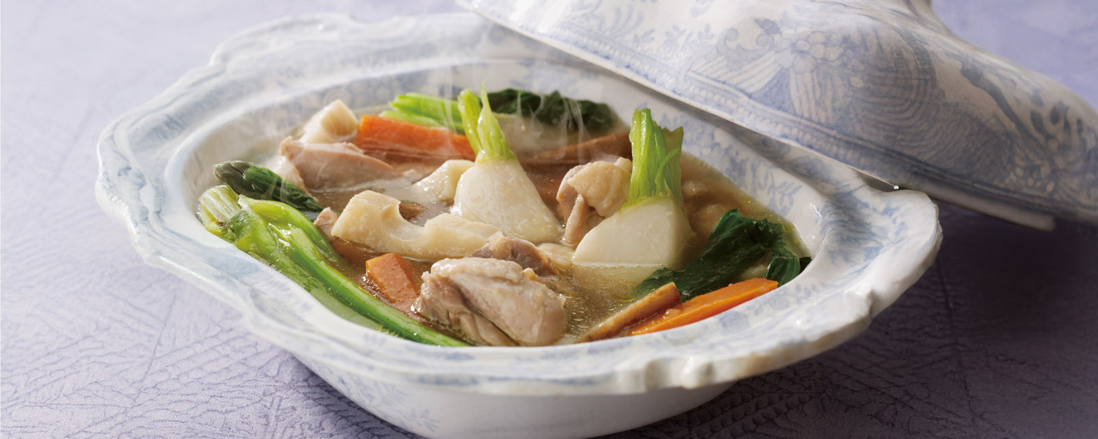 Steaming pot-au-feu with chicken thigh and root vegetables served in a covered ceramic dish.