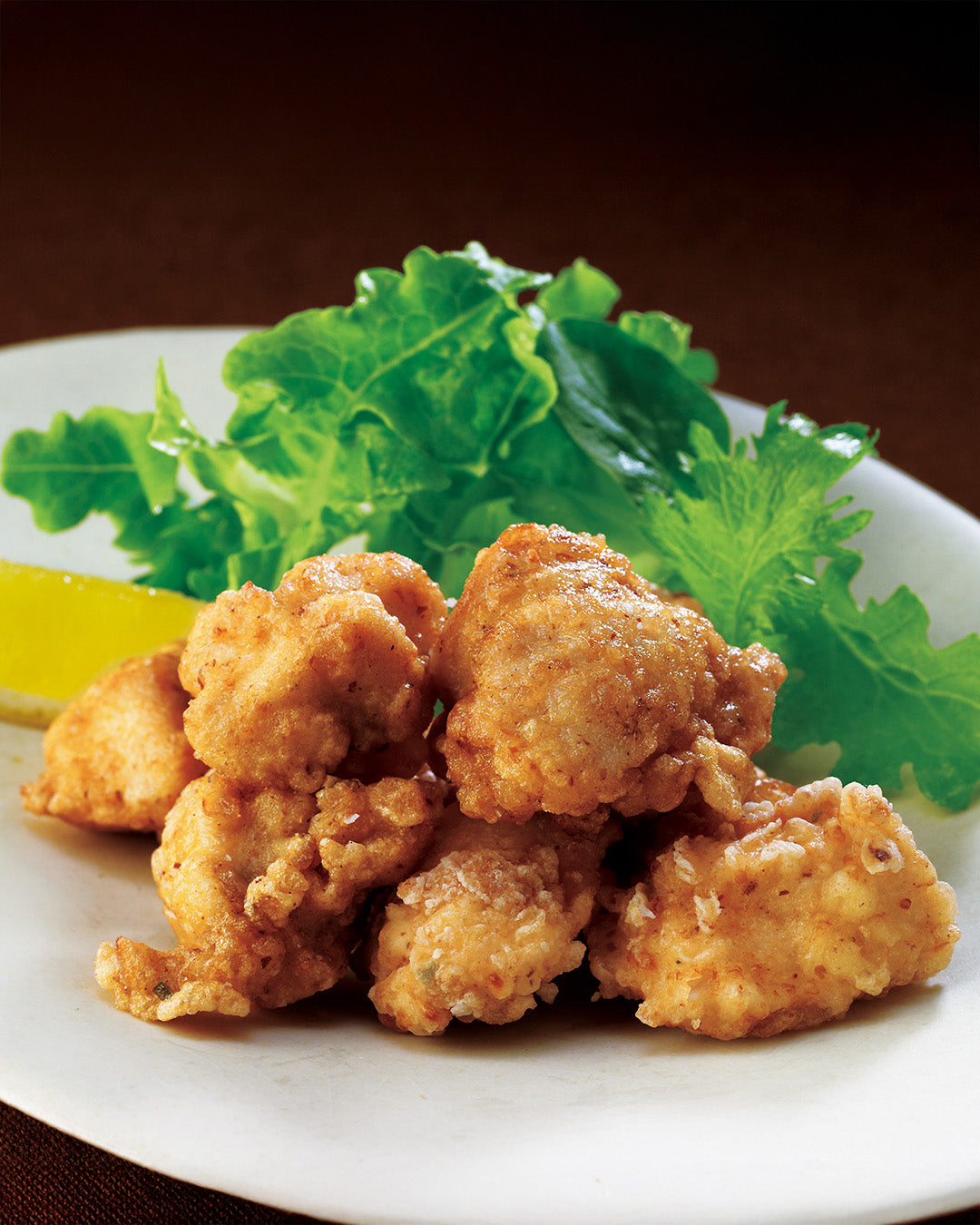Fried chicken pieces on a white plate with a lemon wedge and lettuce leaves.