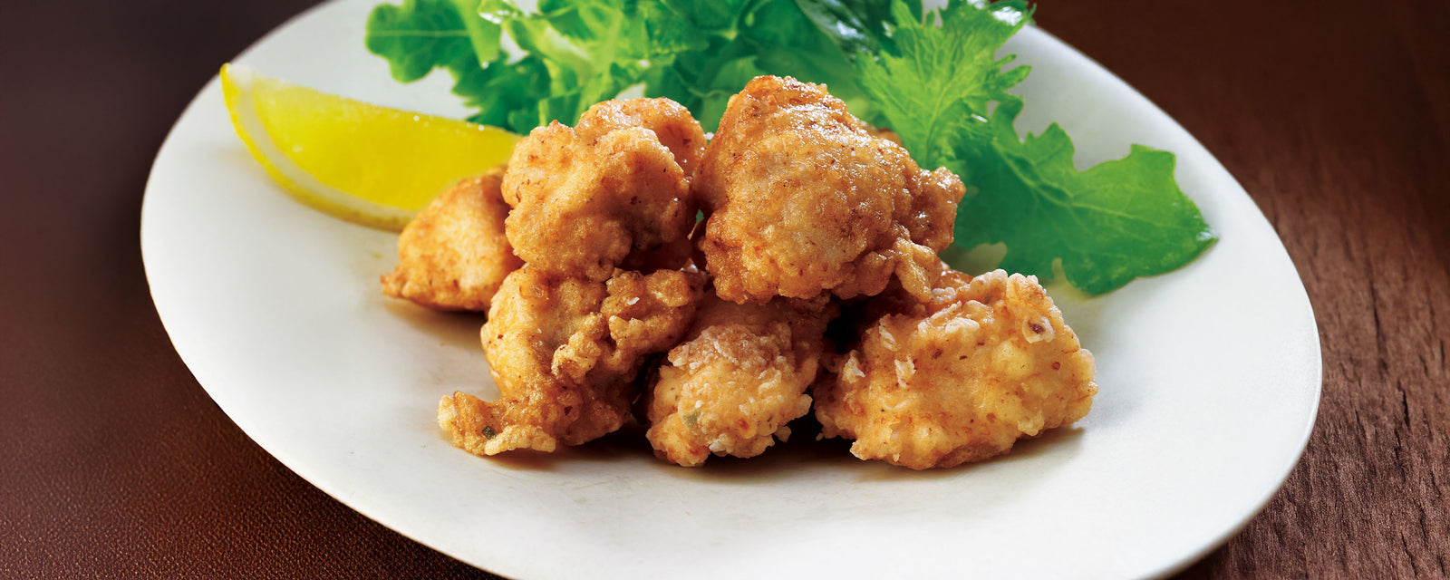 Fried chicken pieces on a white plate with a lemon wedge and lettuce leaves.